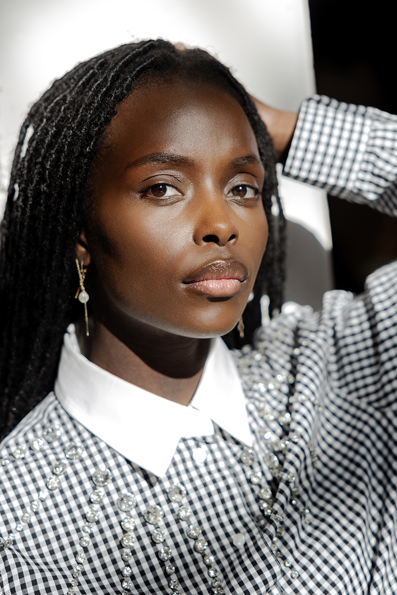 A woman brushing her hair back, wearing a plaid shirt adorned with crystals