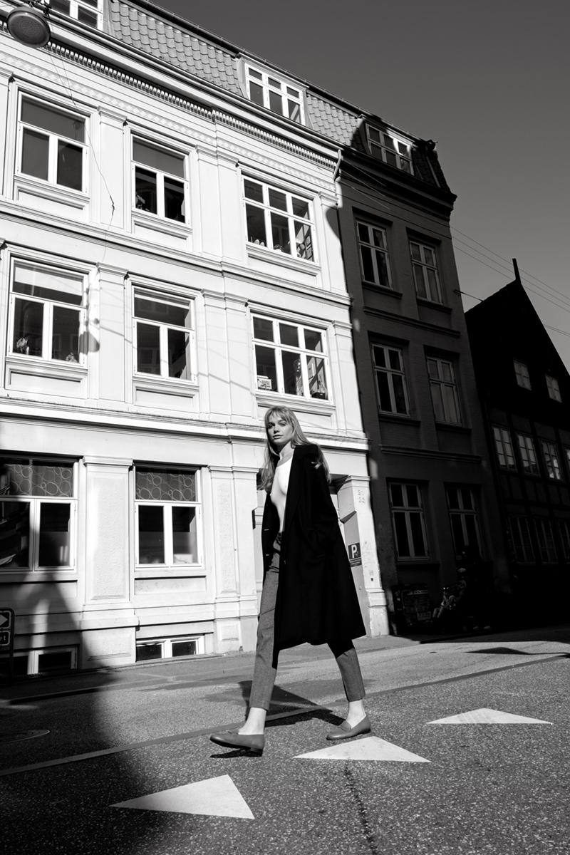 A woman in a black coat walking on the sidewalk against the backdrop of a townhouse