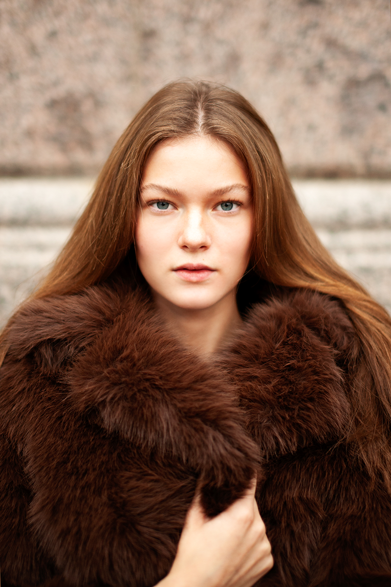 A woman in a brown faux fur coat holding onto the collar