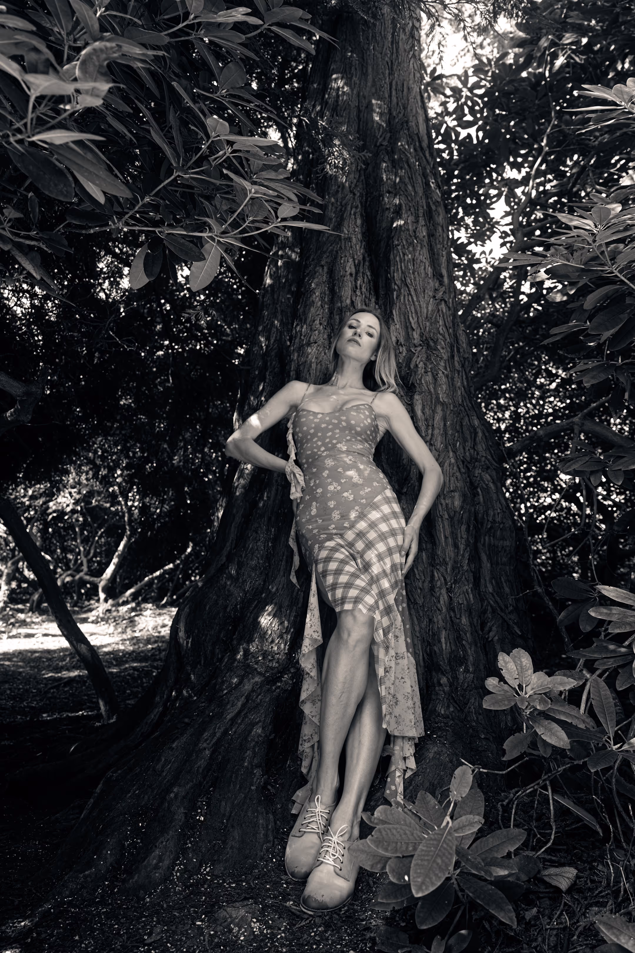 A woman in a dress, in an artistic pose, leaning against a tree.