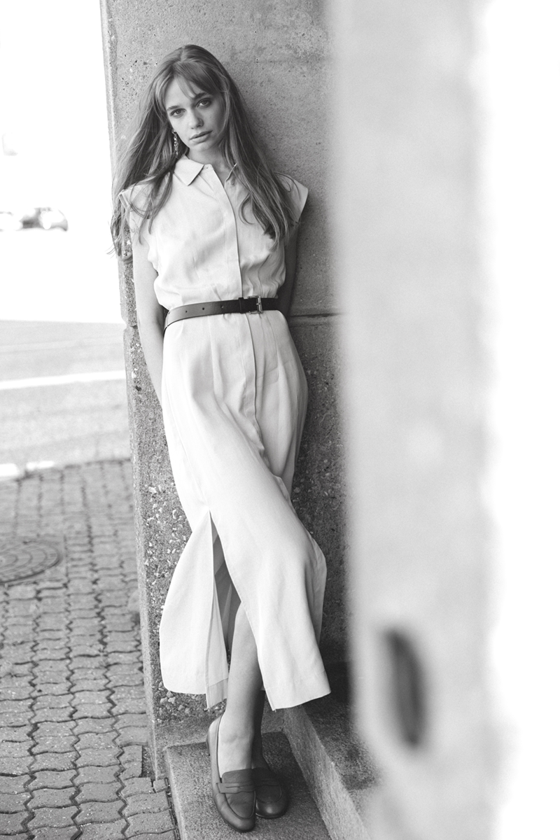 A woman in a dress leaning her back against a townhouse door frame