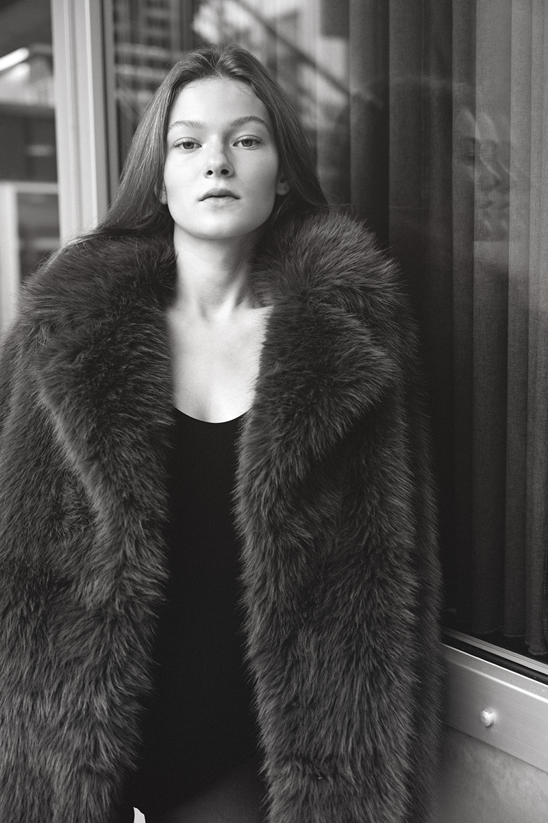 A woman in a faux fur coat and bodysuit against a window display