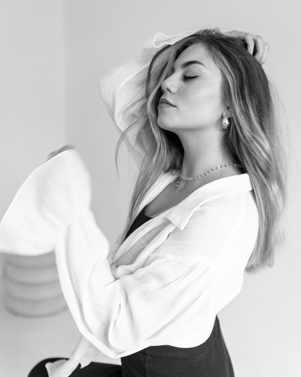 A woman in a white shirt, brushing her hair back