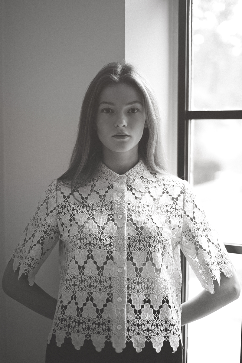 A woman in an embroidered blouse standing by a window