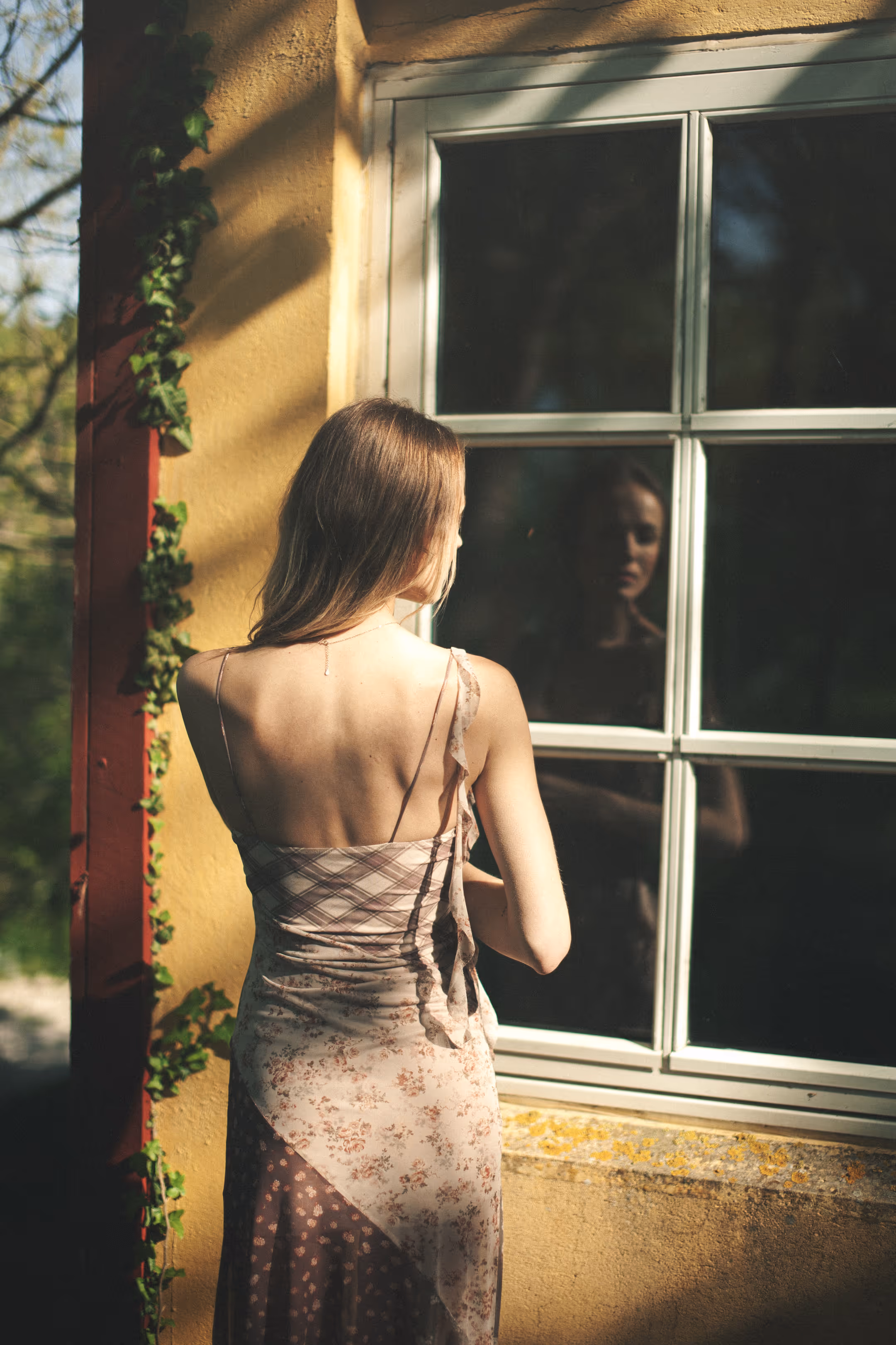 A shot of a woman standing with her back turned, looking out the window of a house.