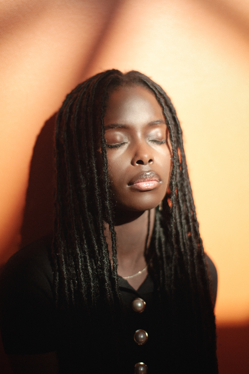 A woman with closed eyes leaning against an orange wall