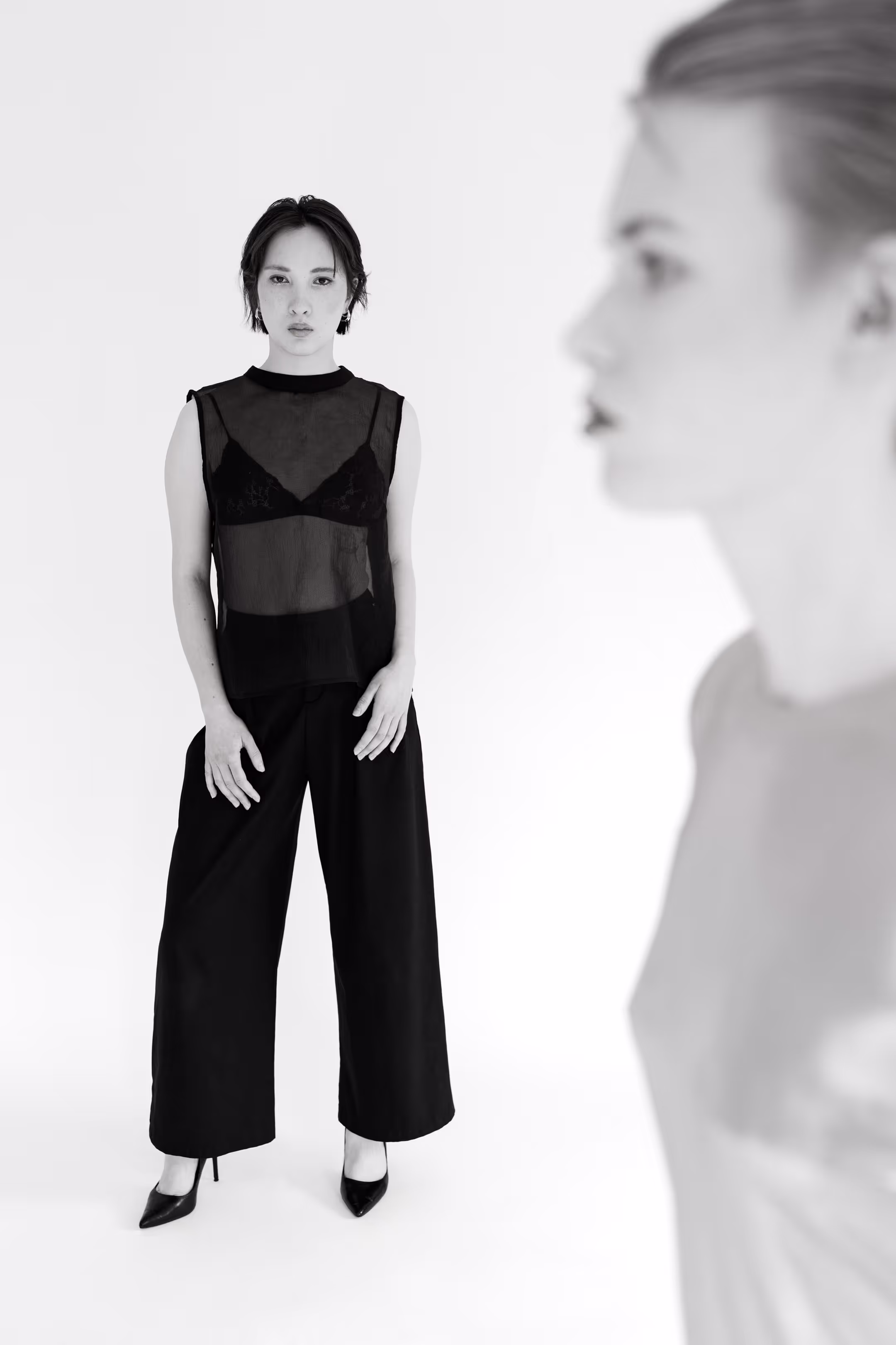 Two women in a minimalist space; one clear in the background, the other blurred in the foreground