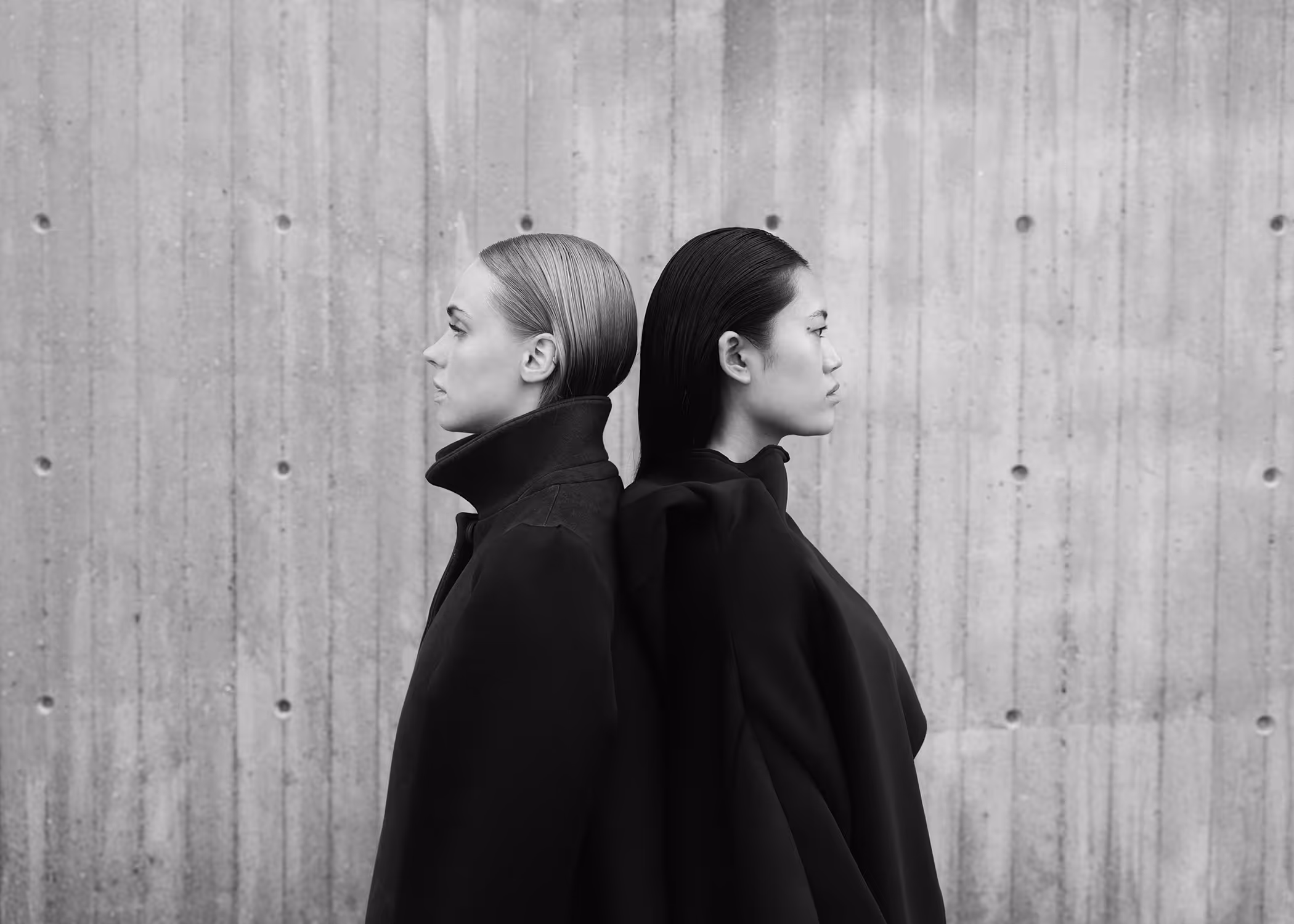 Two women standing by the wall back to back facing away from each other