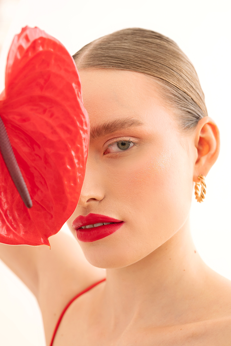 Woman covering one eye with an anthurium flower