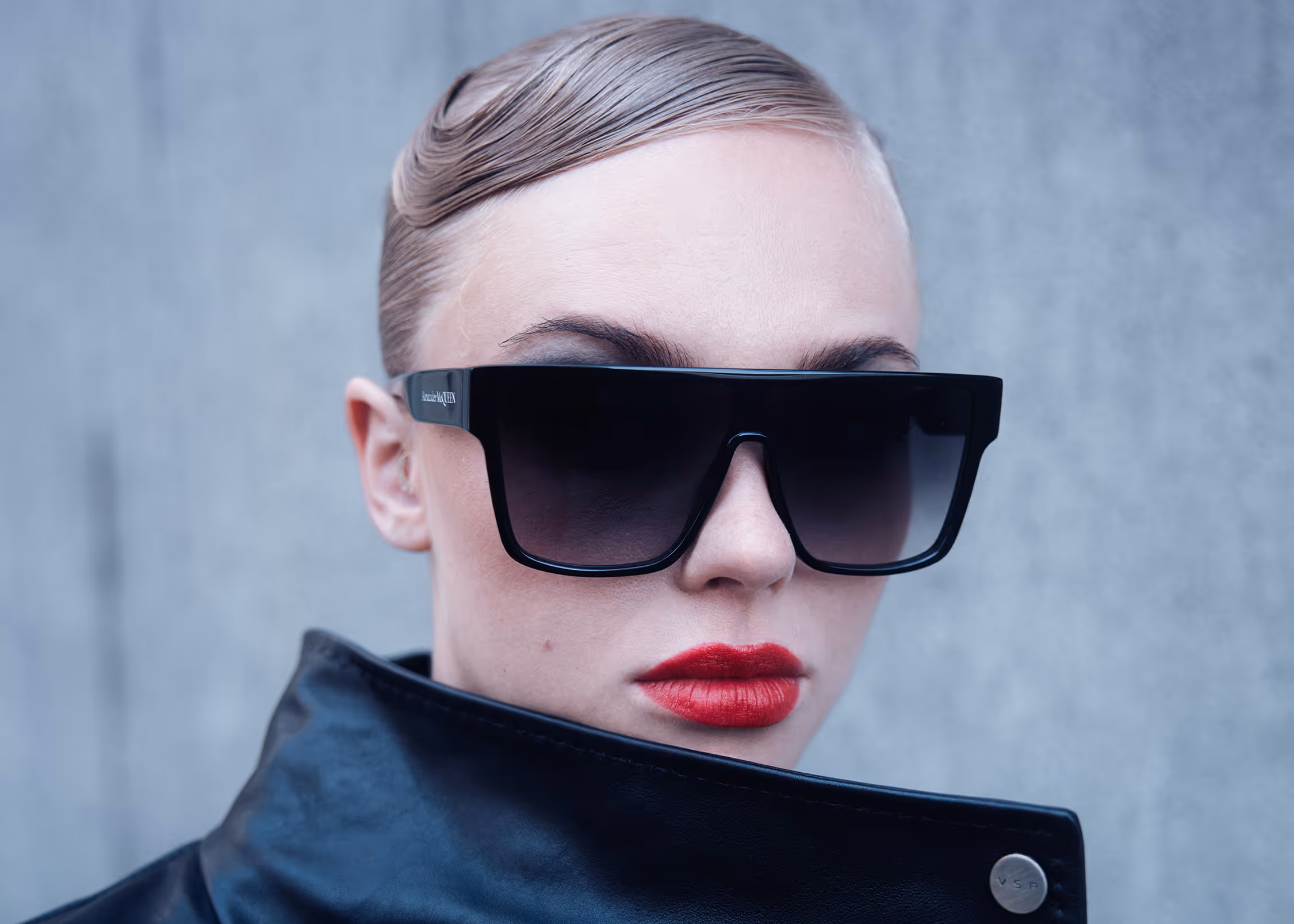 Woman in sunglasses covering her chin with the collar of a black leather jacket