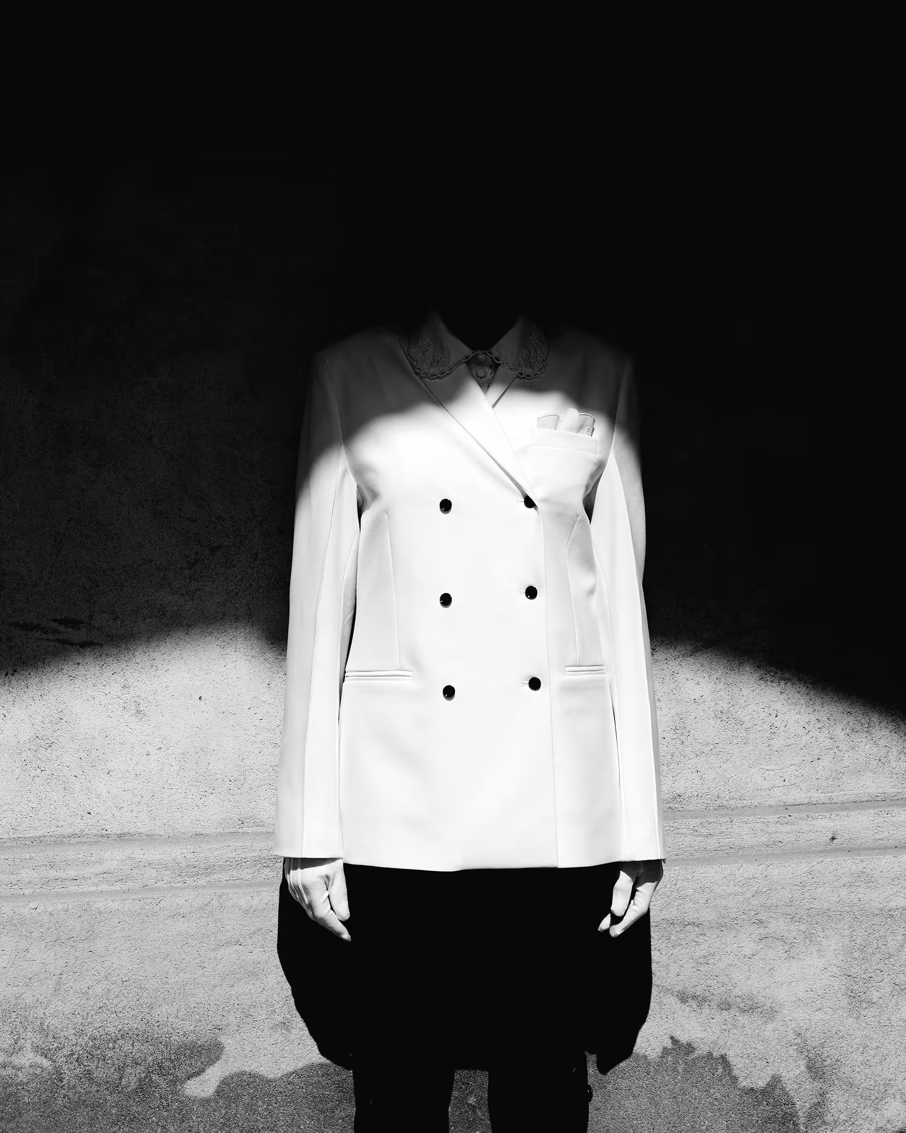 A woman standing by the wall with her head cast in shadow