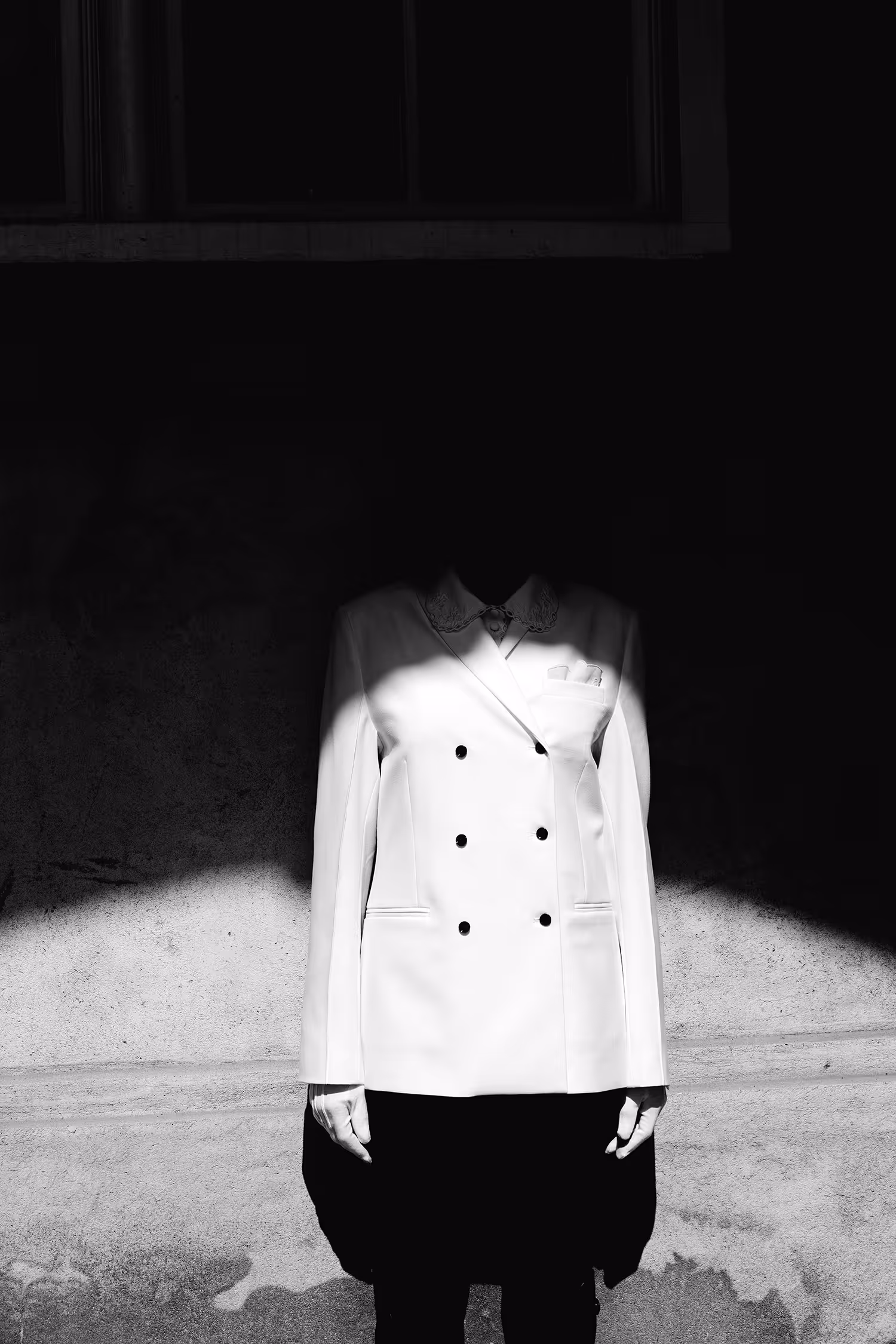 A woman standing by the wall with her head cast in shadow
