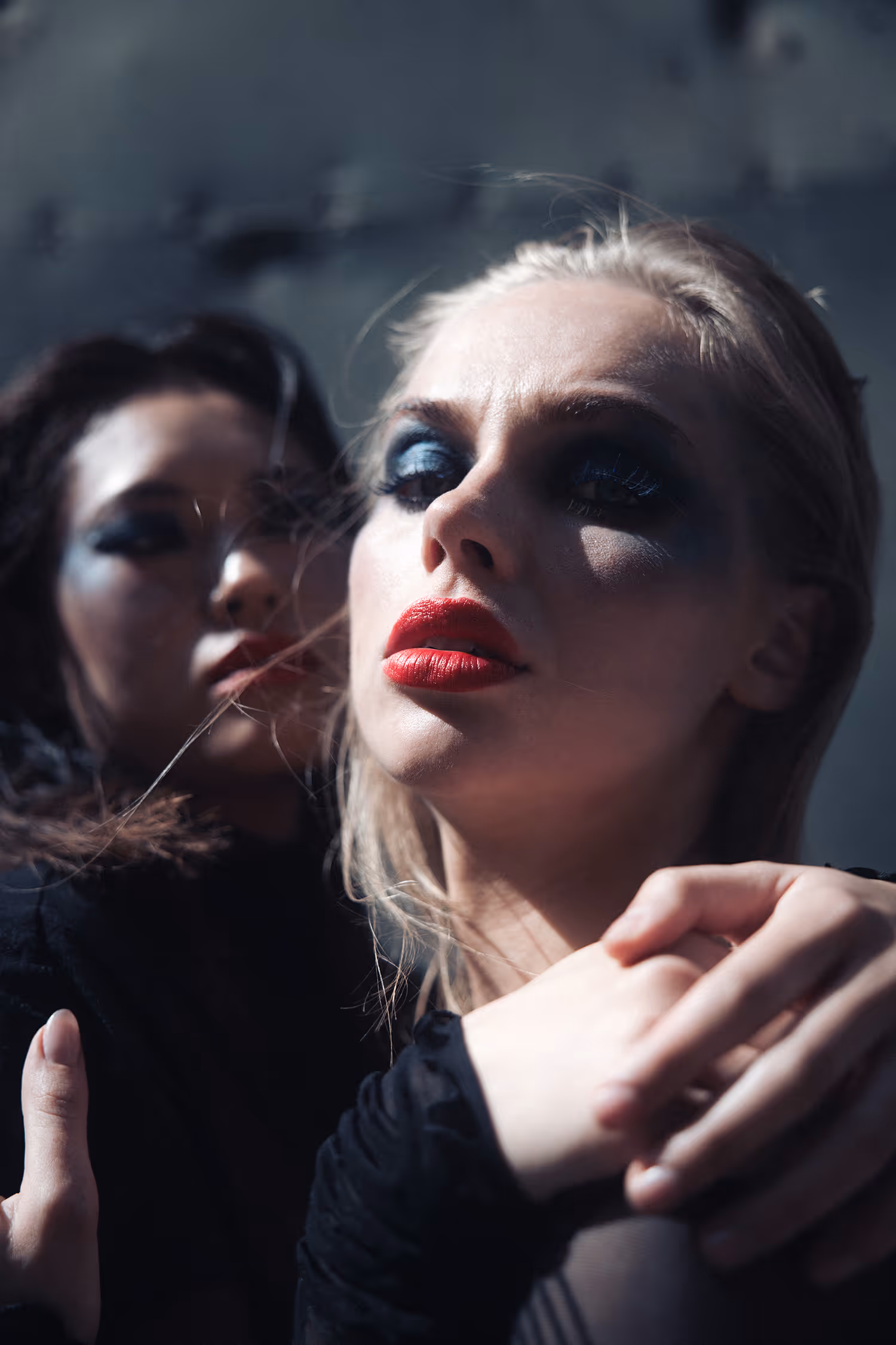 Close-up beauty shot from 'Monolit' editorial in Aarhus. Two models with heavy punk makeup and red lips are captured in dramatic hard light with high contrast shadows.