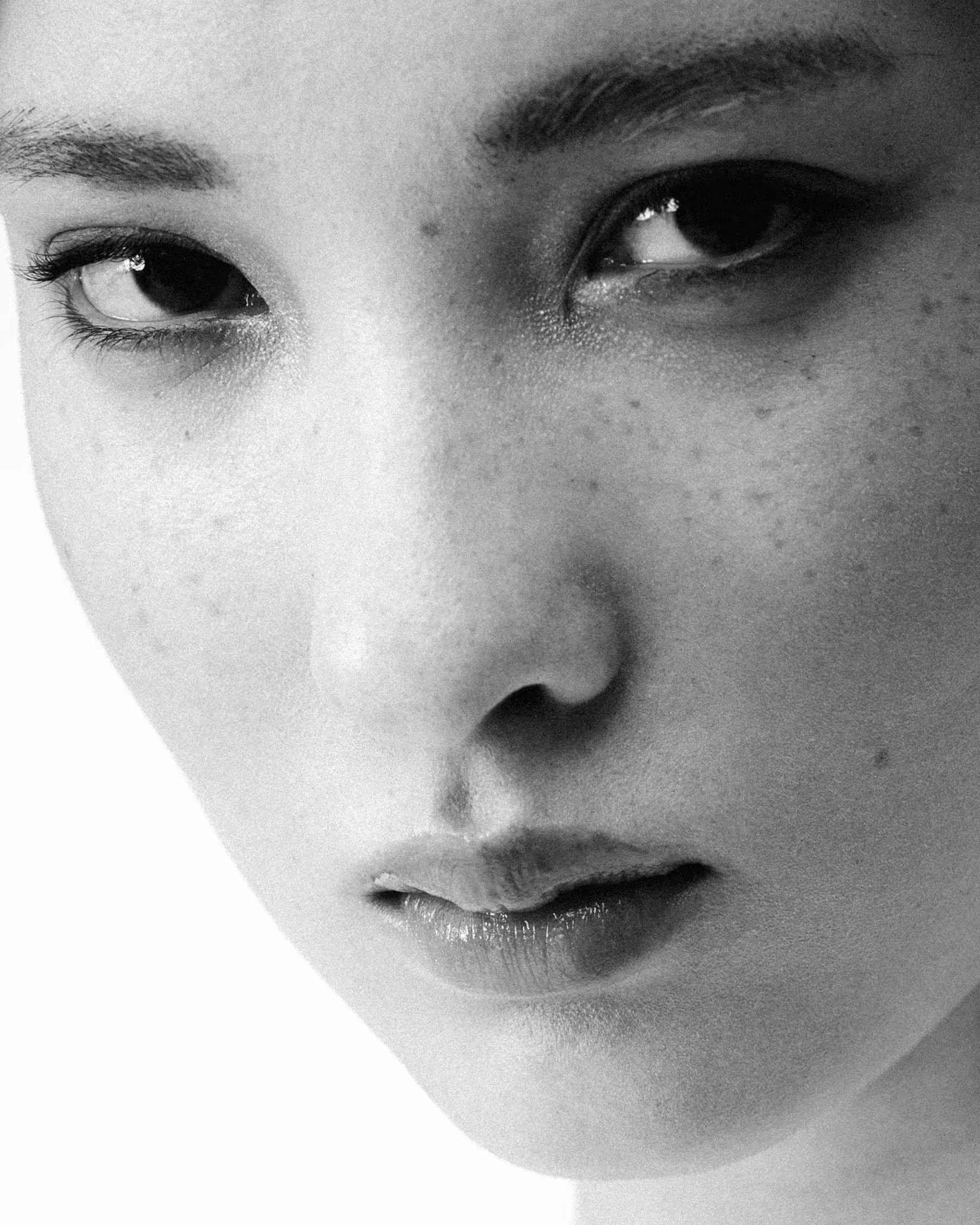 Black and white beauty portrait close-up of a model's face with visible freckles, shot in a studio.