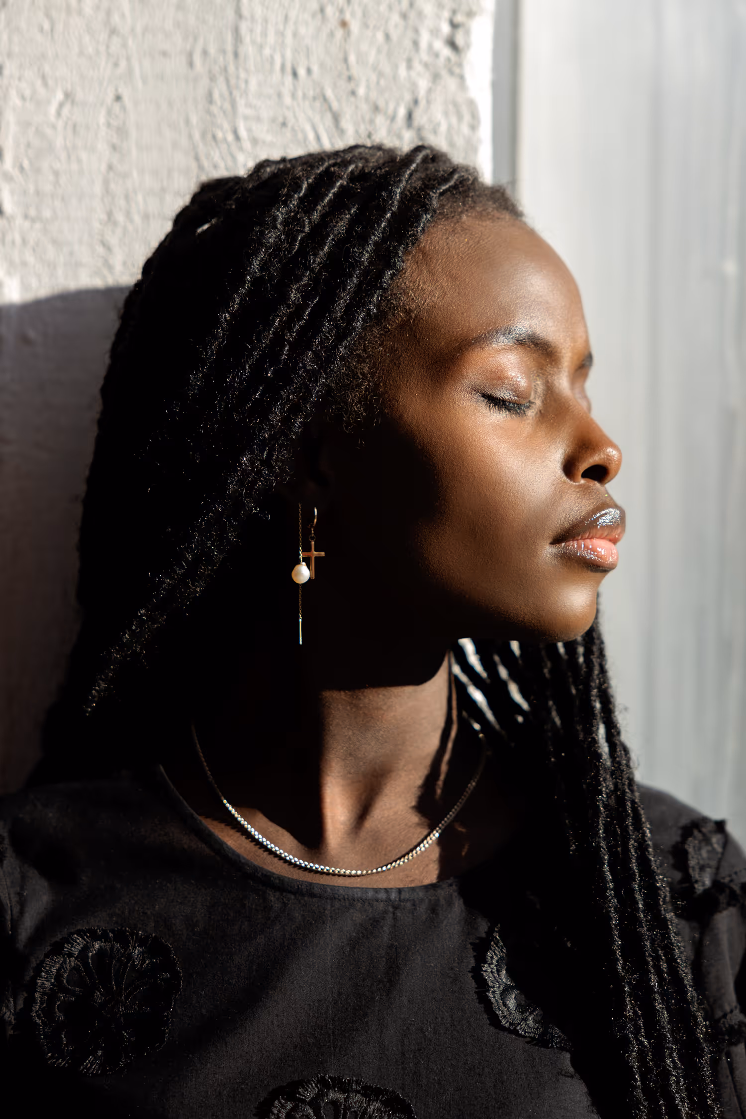 High-contrast beauty portrait of a Black model with braids, captured at Spinderihallerne, Vejle. Sharp directional sunlight highlights the richness of her skin texture and intricate details of her jewellery.