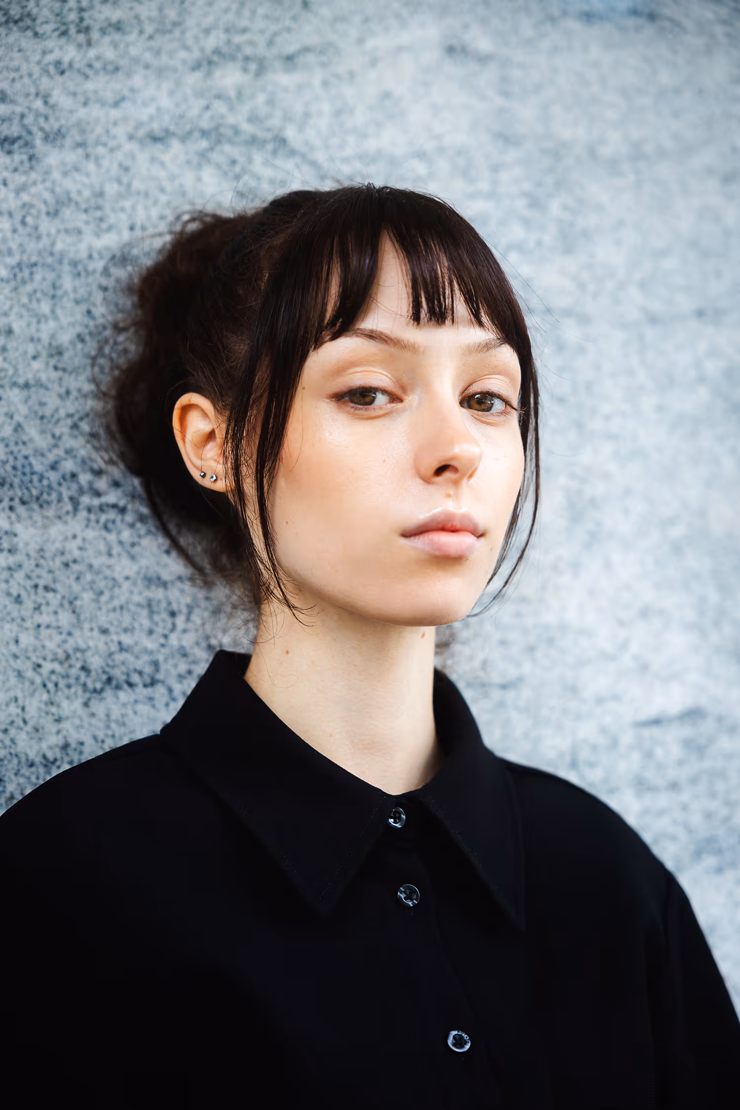 Close-up beauty portrait in Innsbruck. A model with dark bangs and a natural look poses against a grey textured wall in soft, diffuse light.
