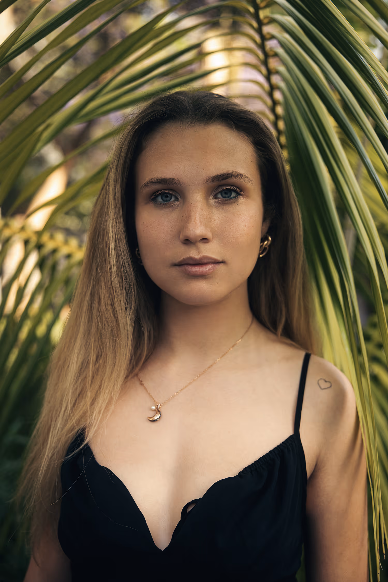 Close-up portrait shot in Madeira featuring a model with visible freckles against a textured palm leaf background in soft, natural light.