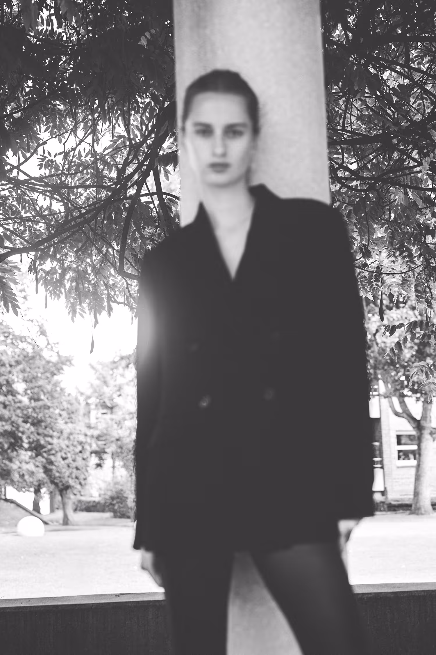 Atmospheric, soft-focus black and white fashion portrait of a model in a blazer leaning against a column in Byparken, Vejle.