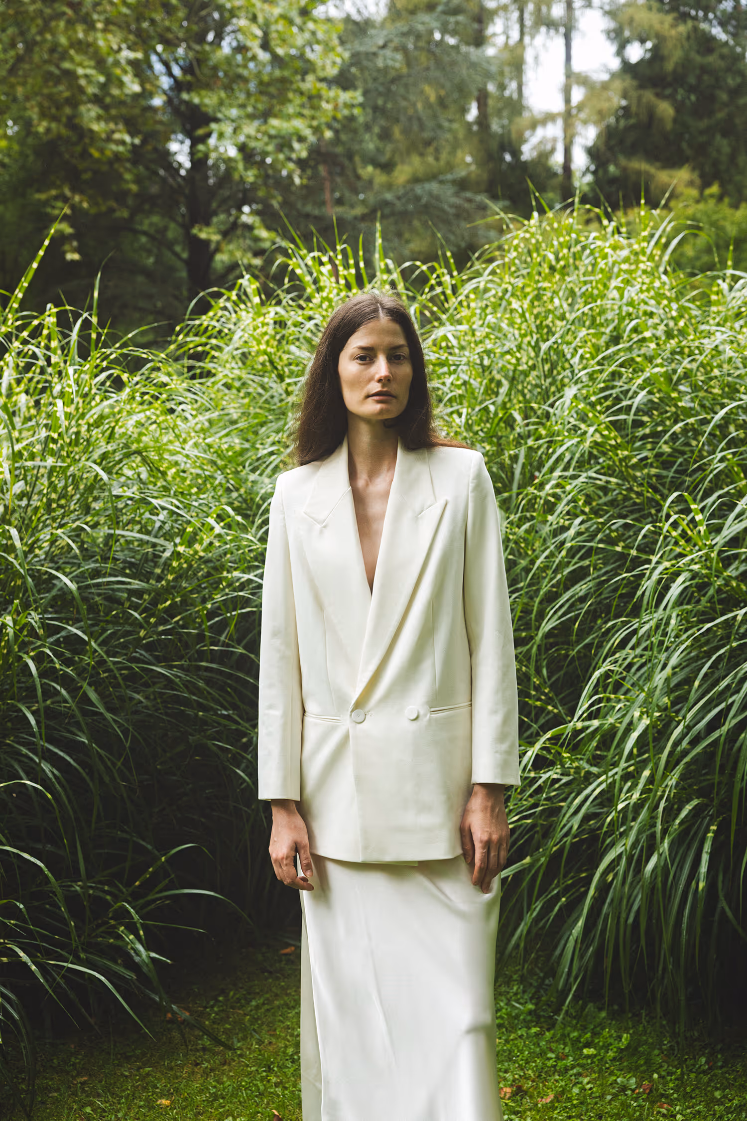 Editorial portrait of Viktoria Machajdik styling a white double-breasted blazer over a long dress amidst lush tall grasses in Innsbrucker Hofgarten.